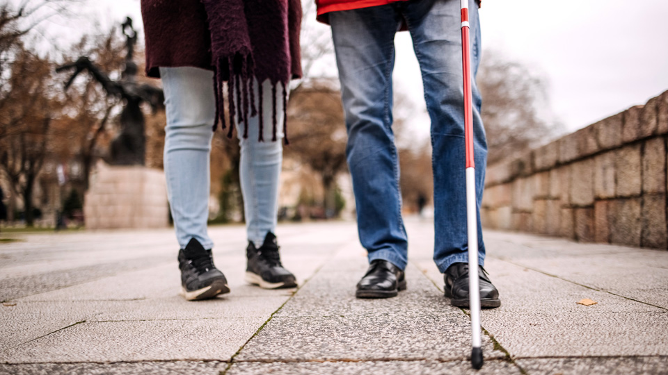 Young female adult spending time with blind old person outdoors on winter day and walking together