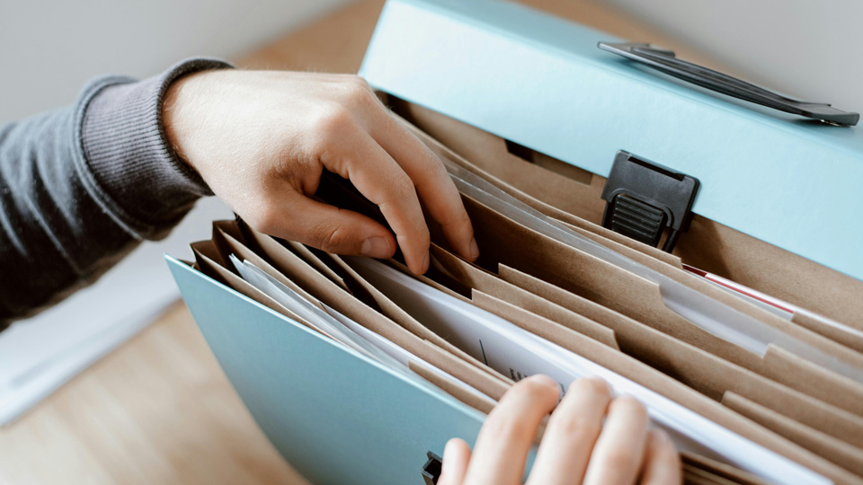 A person rifles through a pale blue folder box of files