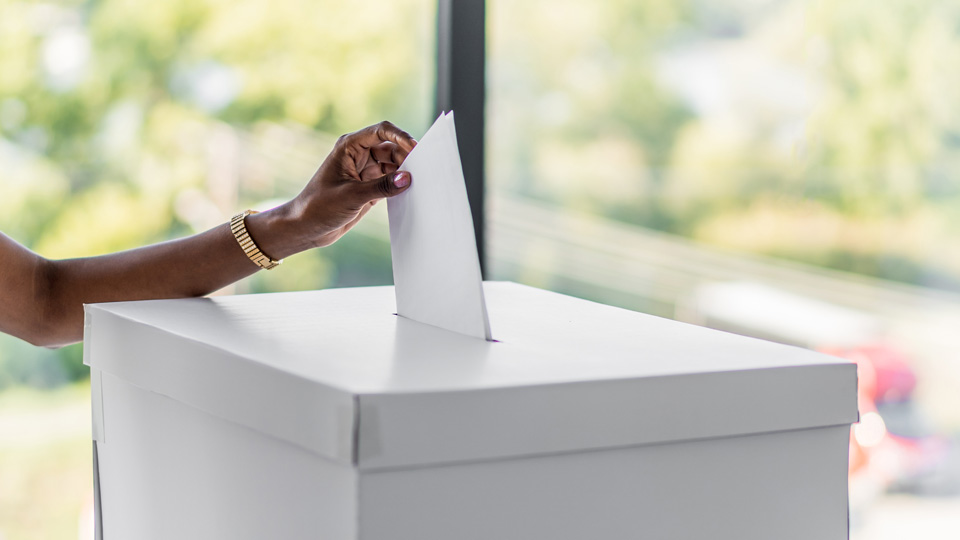 Female hand posting a vote into a ballot box
