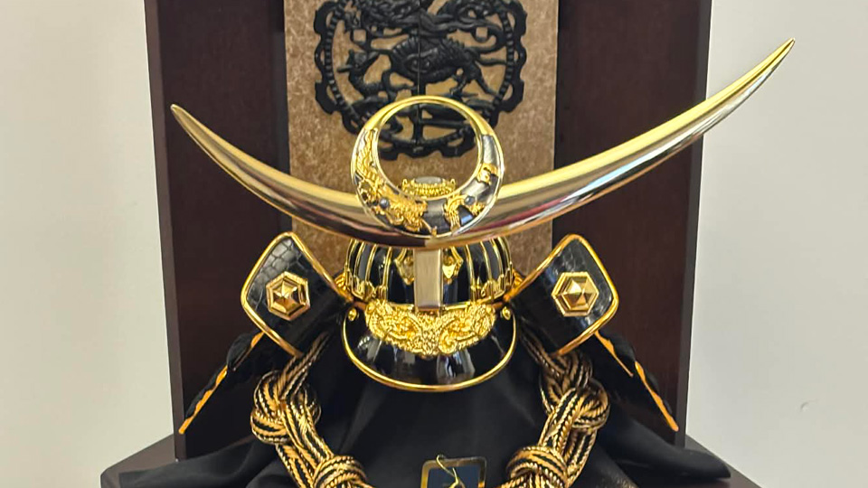 A golden and black samurai helmet displayed in a dark wood case