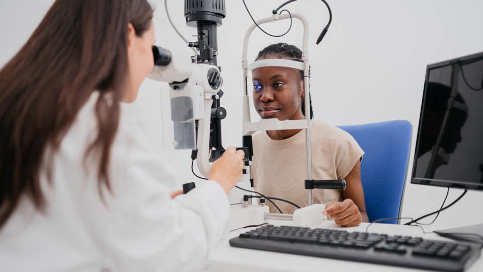 A female optometrist performs a sight test with a slit lamp on a patient