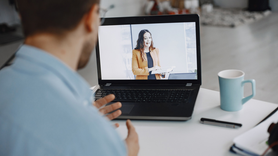 A man watches a live feed of a professional giving a presentation