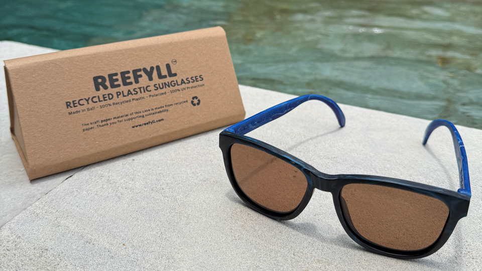 A pair of dark blue sunglasses arranged on the side of a pool with a recycled glasses case beside it