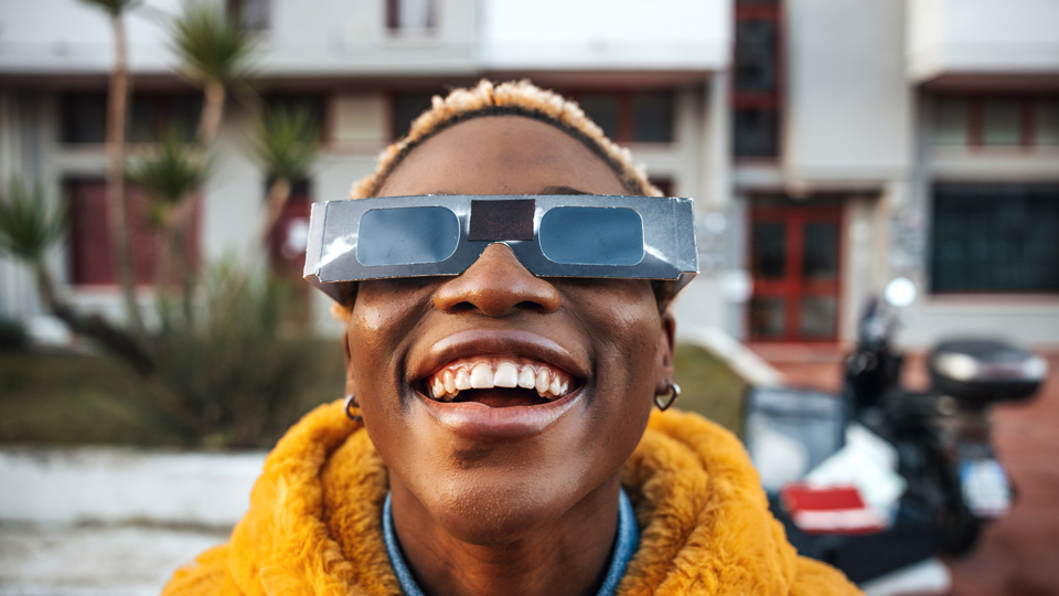 A woman smiles while wearing solar eclipse glasses