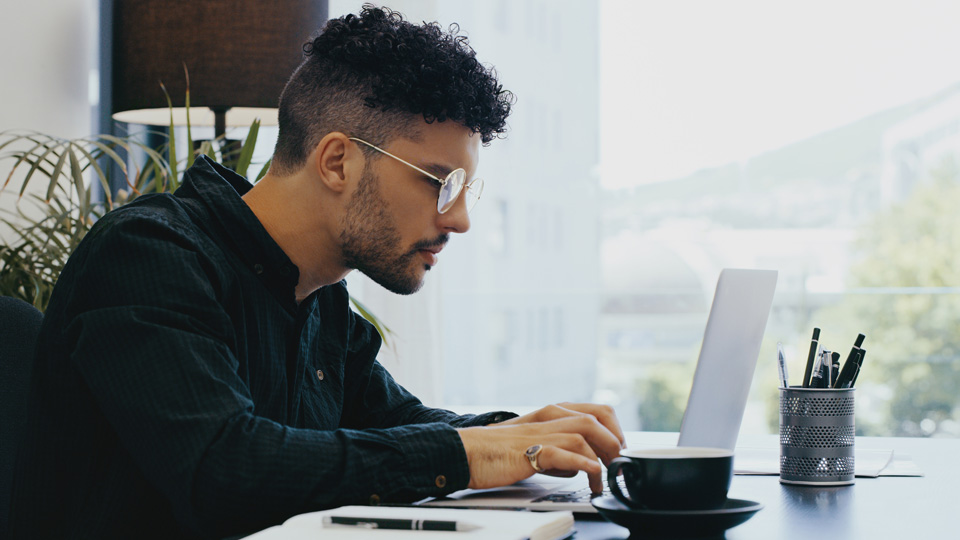 A man sits at a desk working at a laptop