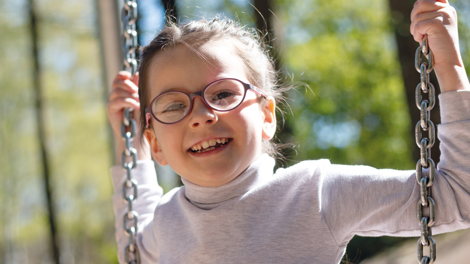 A young girl on a swingset. She is wearing glasses with a pink rim