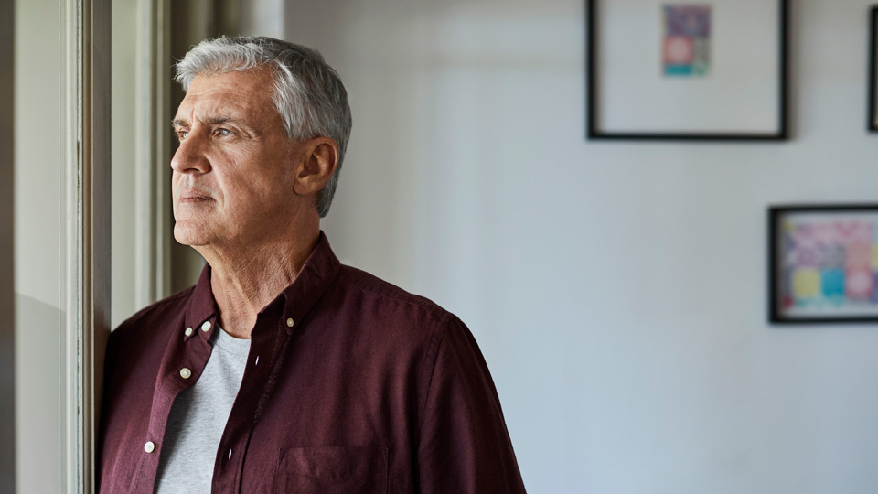 An older man stands looking out a window