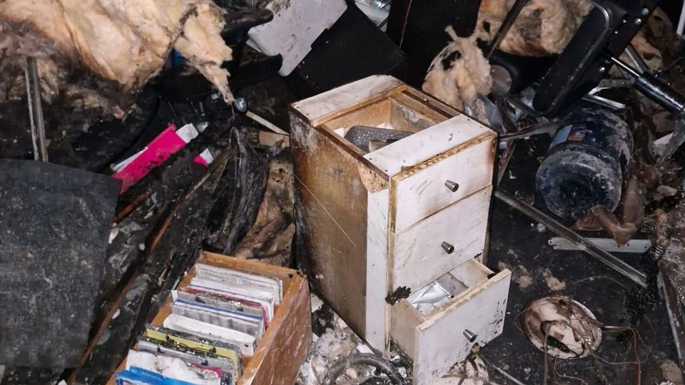 A pile of cabinets, broken furniture, and ceiling insulation piled on the floor and burnt black in places