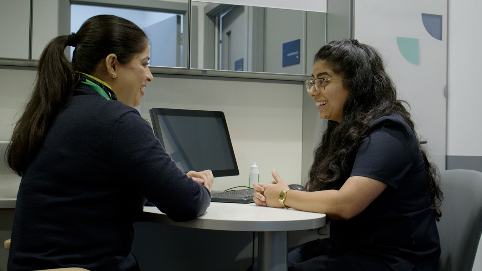Deepali sits talking at a table with a colleague