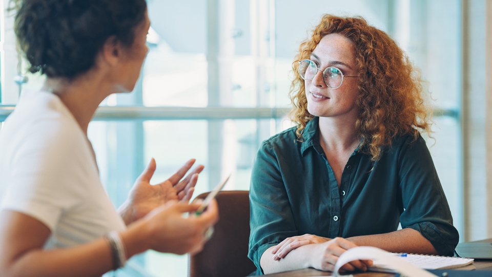 A woman listens to a colleague while seated at a table