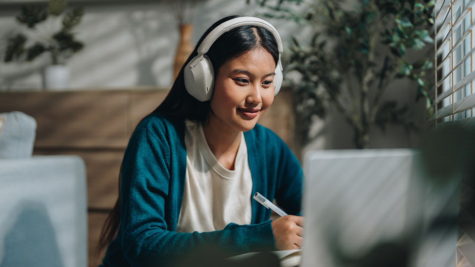 A woman wearing headphones sitting at a laptop smiling