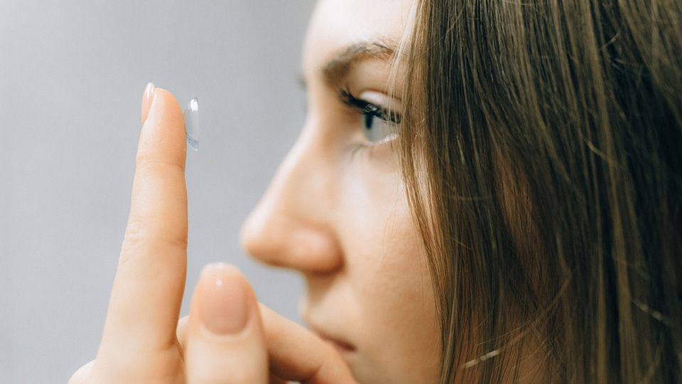 A close-up of a young woman preparing to insert a contact lens