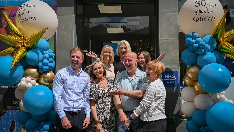 Dr Scott Mackie and members of his practice team standing outside of the practice with ballons all around them and the practice door