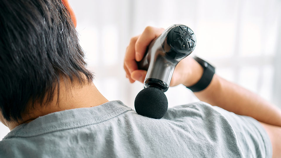 A man uses a massage gun on his shoulder