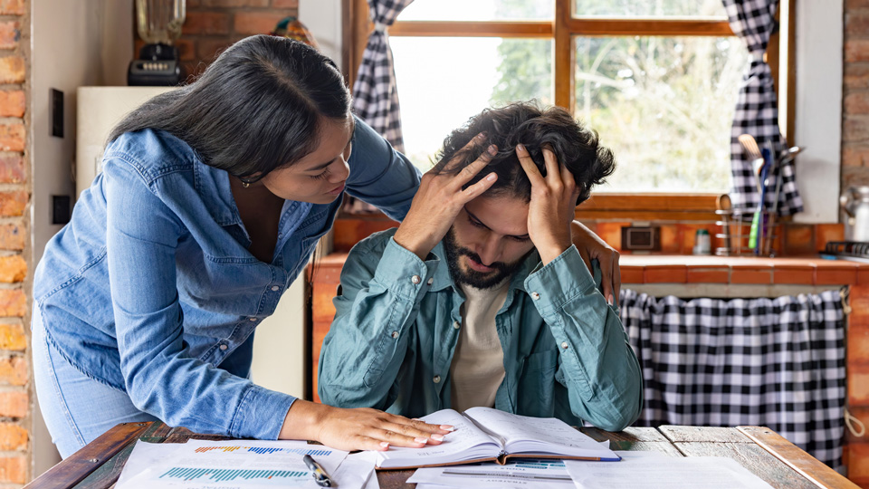 Husband and wife stressed whilst looking at a ledger book at a dining table