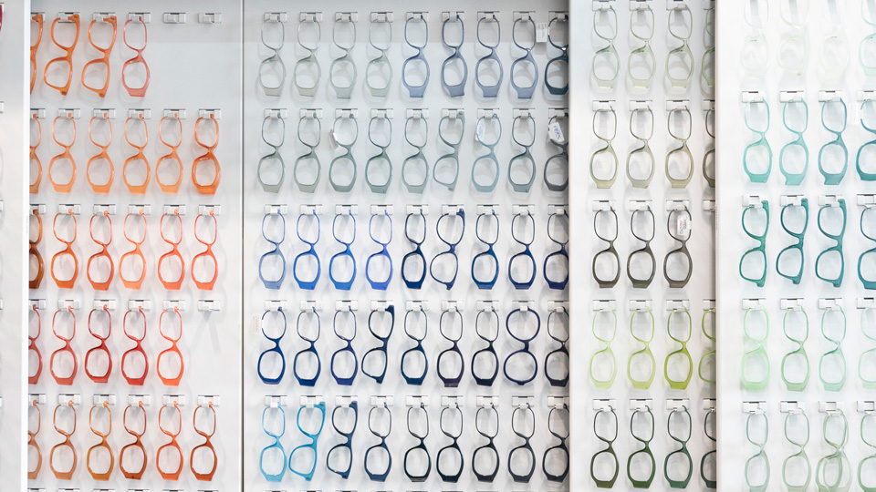 Rows and rows of glasses frames in production arranged in a rainbow of colours from red, to orange, greys, blues, and greens