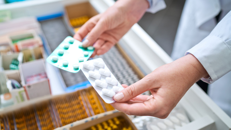 A pharmacist holds medication above a drawer of medication