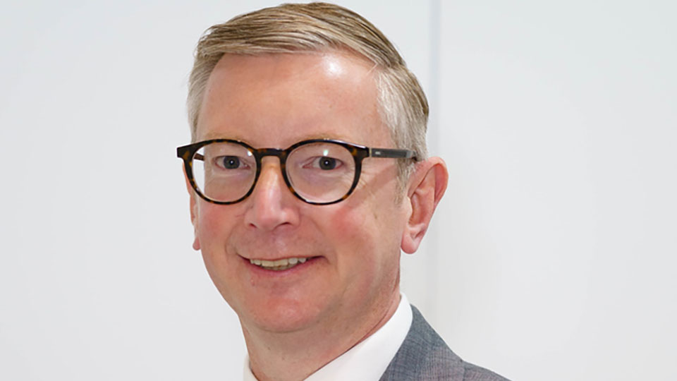 Giles Edmonds wearing a suit looking at the camera smiling