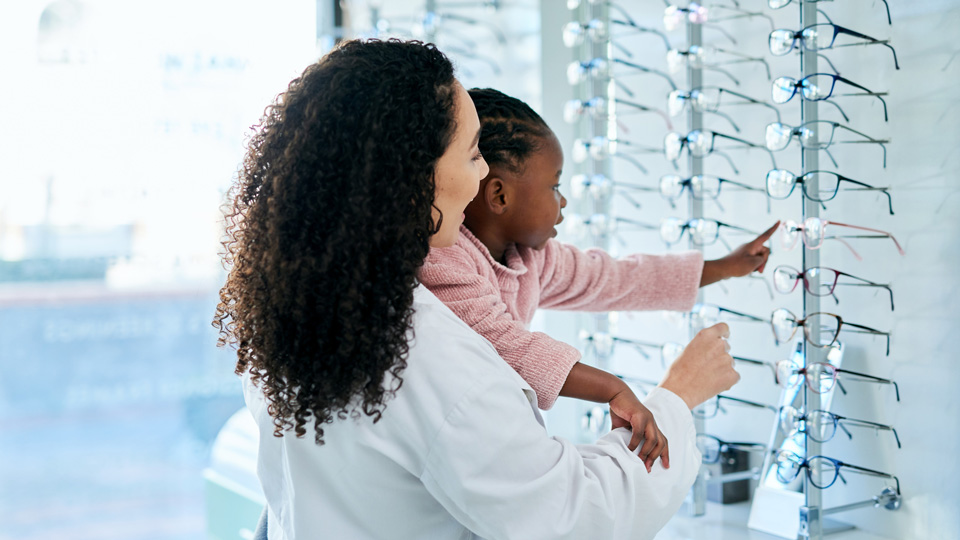 A girl is lifted by a woman to look at a display of glasses on a shelf