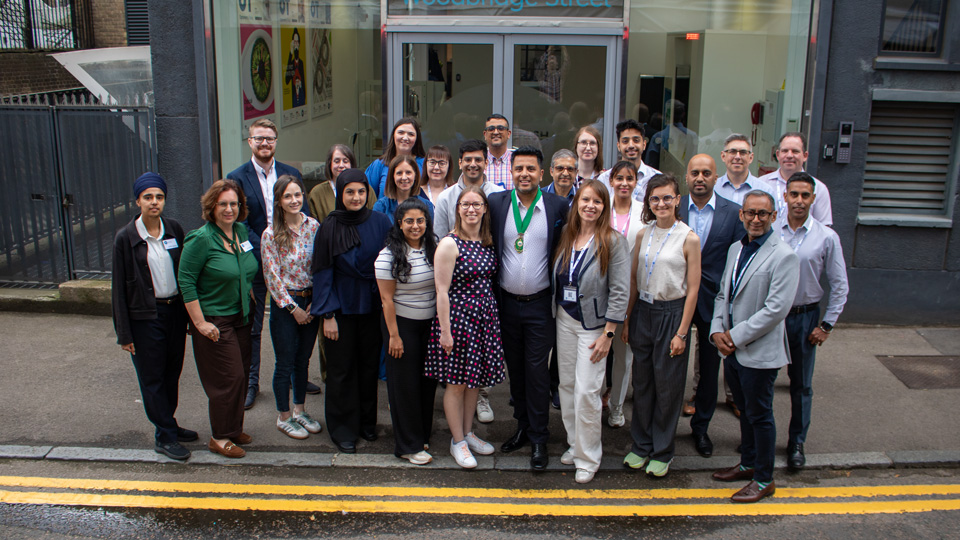 The AOP Councillors gather outside the glass front doors of the building, they are all looking up and smiling towards the camera