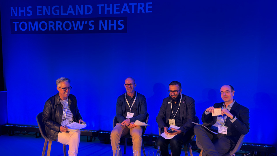 Four people sit in a row on stage, lit by a blue background