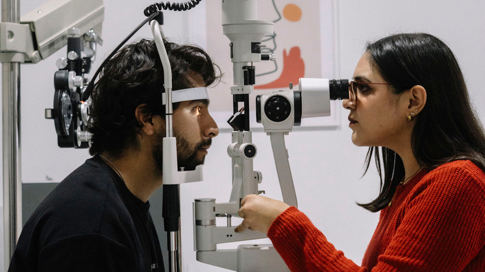 A female optometrist performs a sight test with a slit lamp for a male patient