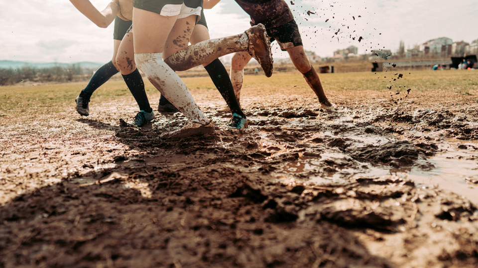 A group of female athletes play rugby on a muddy field