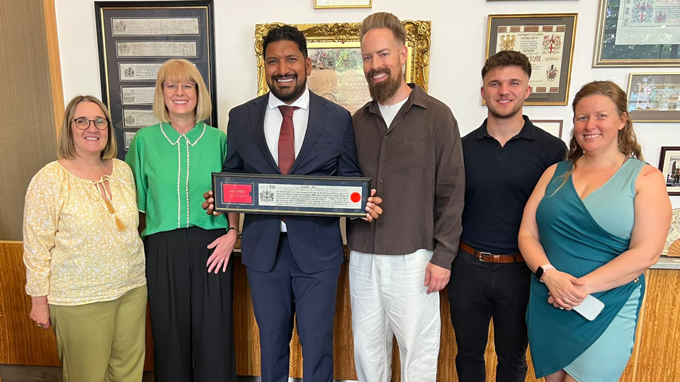 Zabir is surrounded by five people all dressed smartly. He holds the Freedom of the City of London document and they are all smiling