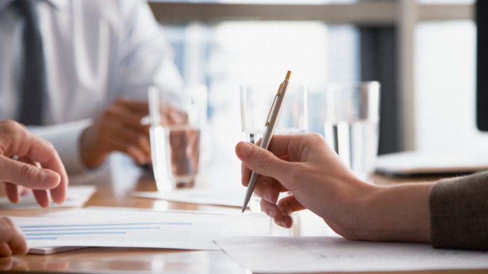 A close up of a document being signed with water glasses in the background