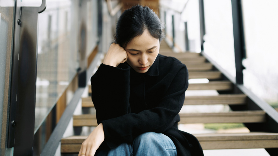A woman sits on the stairs with her head resting on her hand