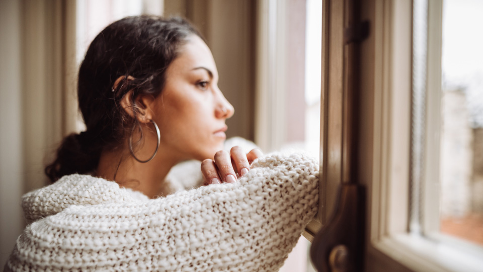 A woman stands at the window looking pensive