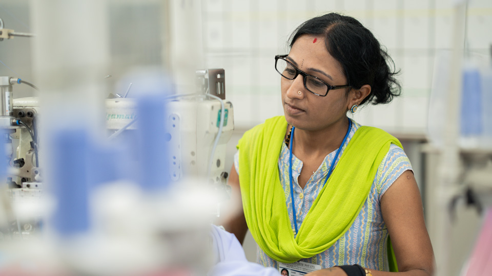 Woman in a yellow sari and glasses at a sewing machine
