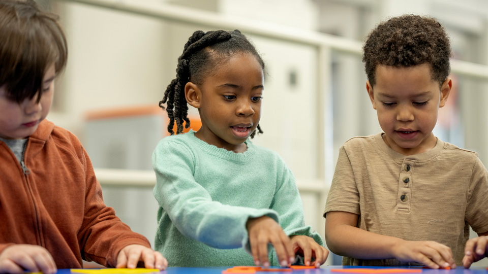 Three children play with coloured shapes on a table