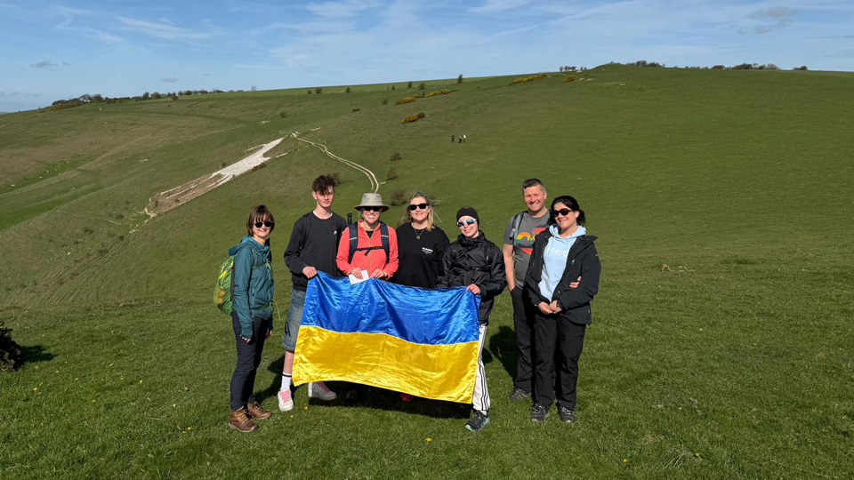 Walkers hold the Ukraine flag and pose on a sunny green hillside in front of one of the white horse chalk carvings in Wiltshire
