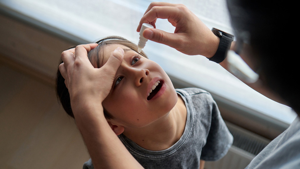 A parent puts eye drops in their child’s eye