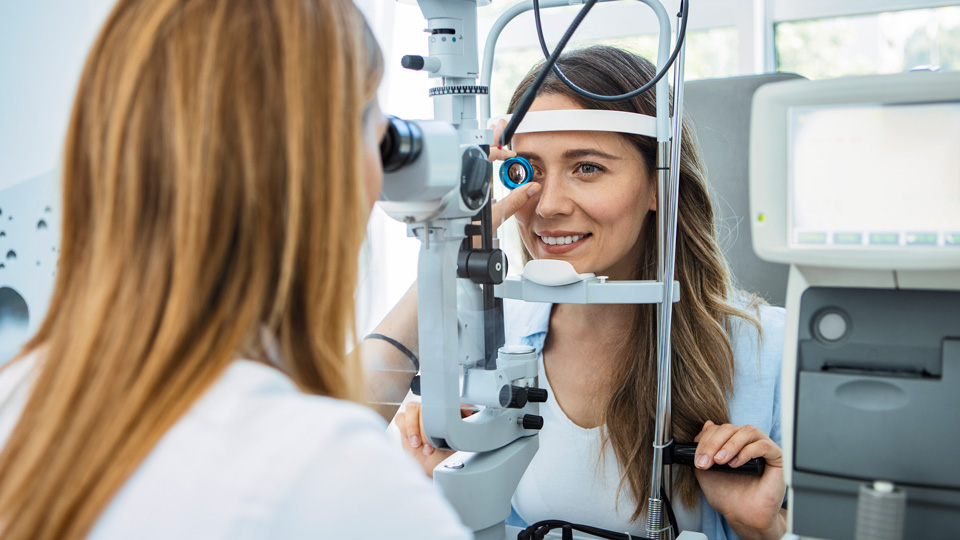 A woman is receiving an eye test. The optometrist holds up a Volk lens to her eye