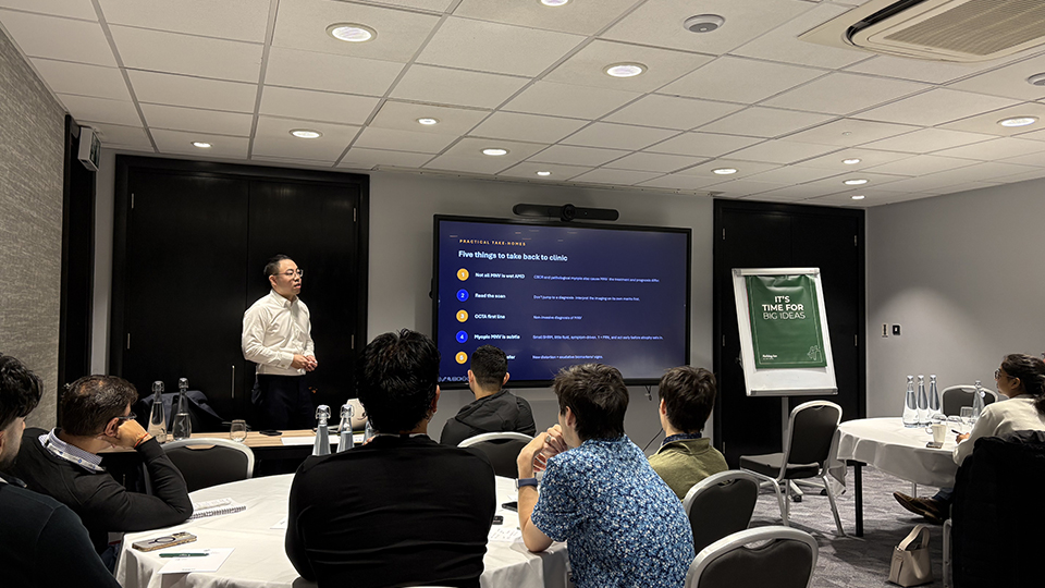 A man presents to a group of seated delegates in a conference room, displaying a slide titled “Five things to take back to clinic” on a large screen
