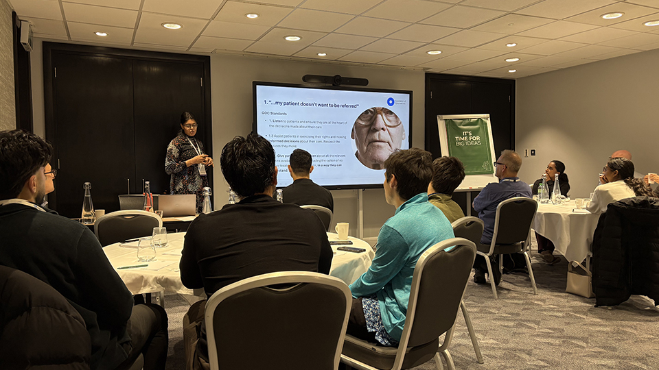 A woman stands beside a presentation screen addressing seated delegates at a professional meeting. The slide discusses a patient who does not want to be referred and includes an image of an older man wearing glasses
