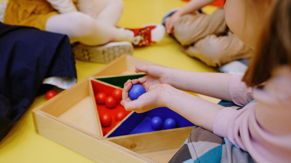 Pre-school children sit around a wooden sorting toy of coloured balls