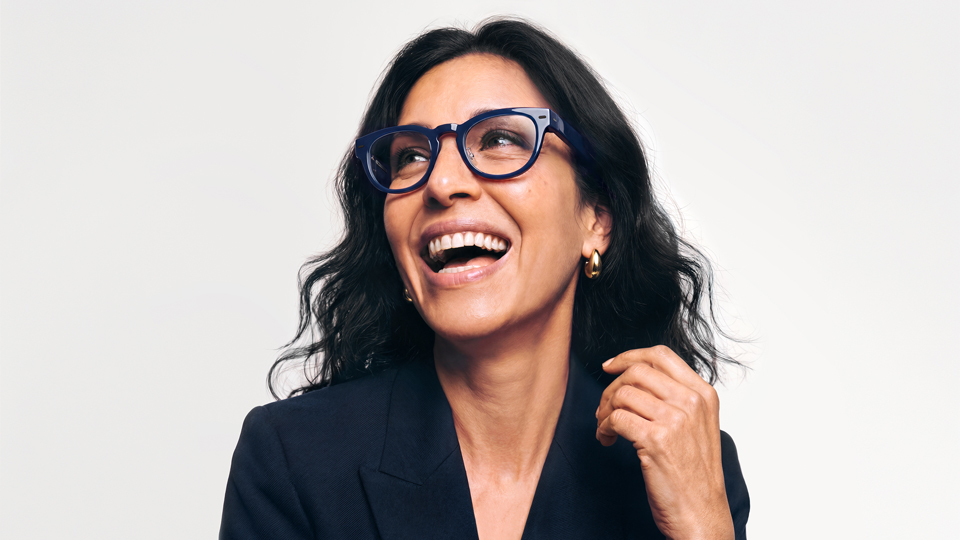 A woman laughs joyfully. She wears dark blue pantos style optical frames