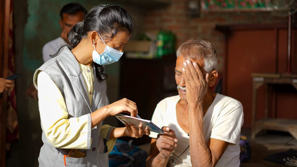 A man covers one eye and reads from a page held by a practitioner in front of him