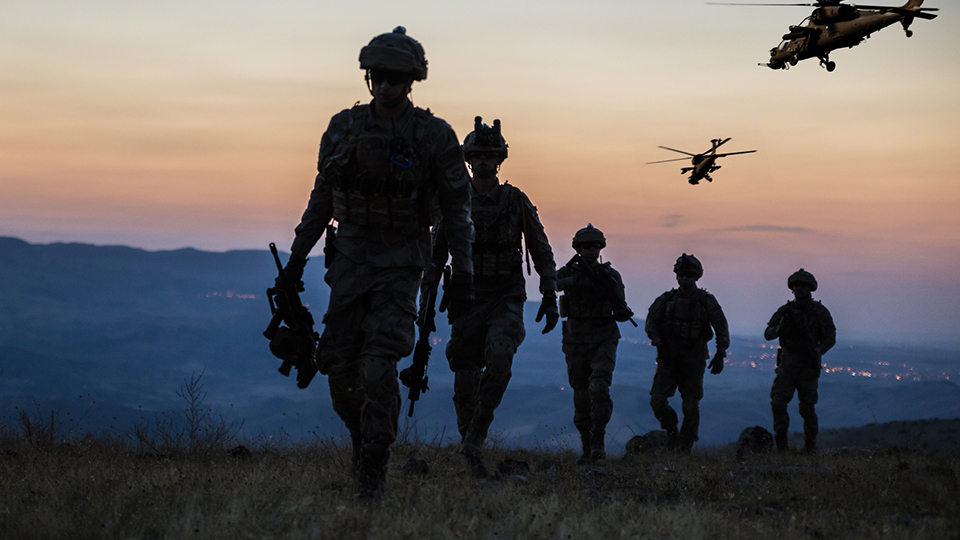 Silhouettes of soldiers and helicopters at dusk