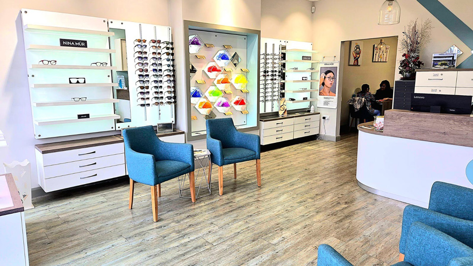 The entrance to Eyewise Opticians with a reception desk and dispensing area arranged with two soft chairs and a small side table. The effect is colourful and warm
