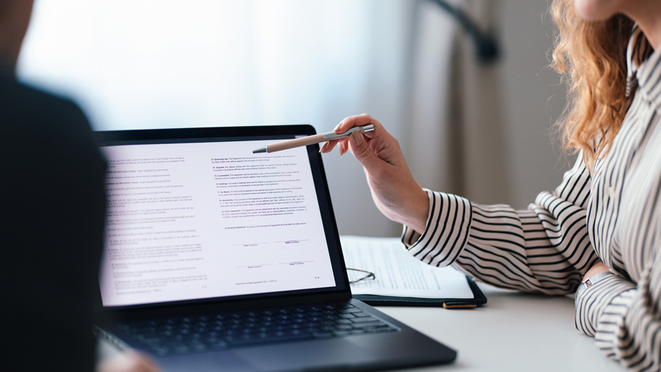 Two co-workers engaged in a business review, examining documents on a laptop screen in a professional setting