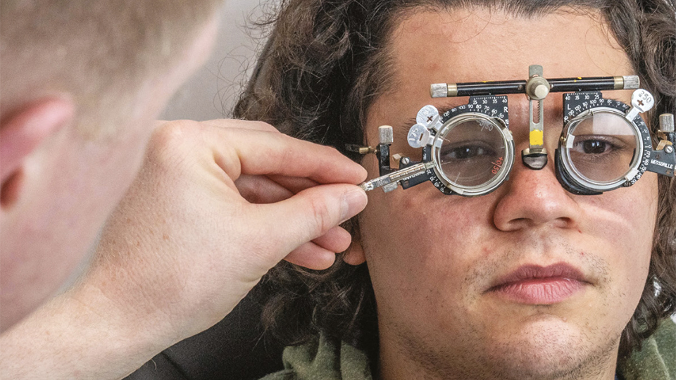 A young man in a green sweatshirt receives an eye test