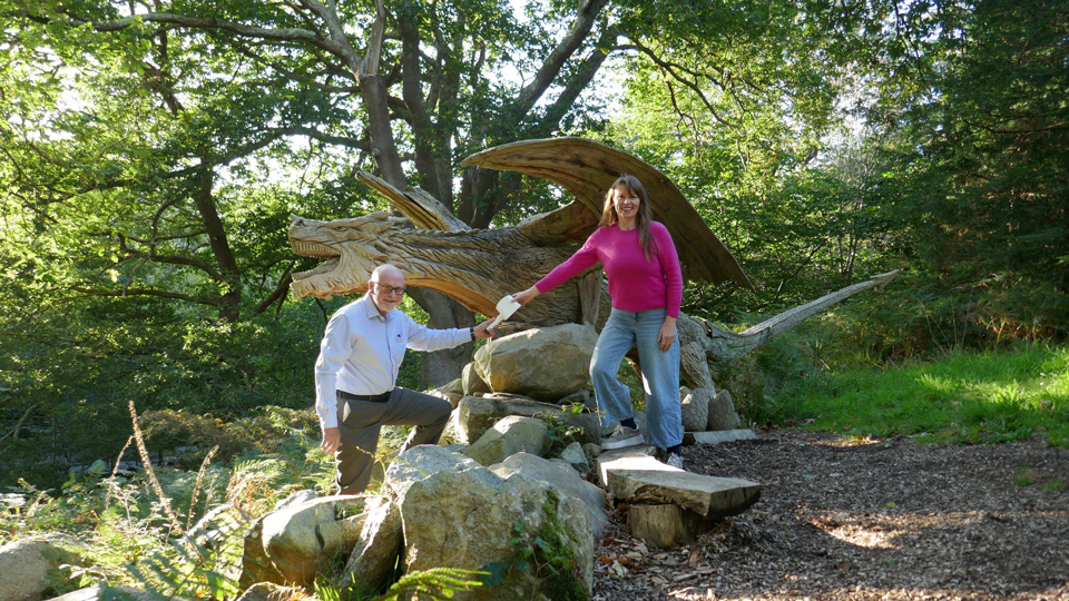 Sarah Lowry and Chris Gould standing outside by a tree trunk on the ground. They are looking at the camera and smiling