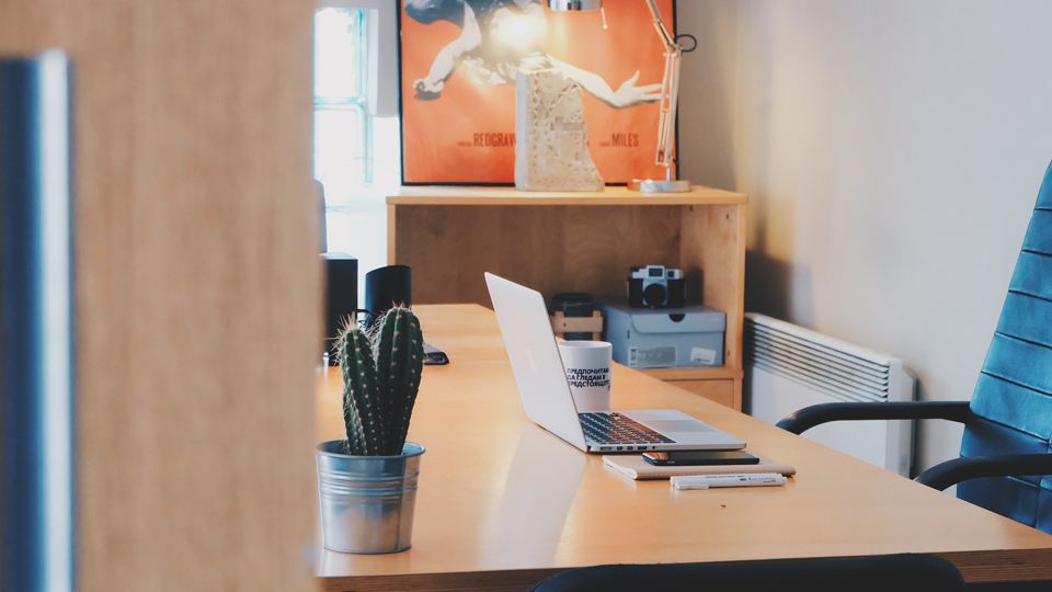 An open office door reveals a quiet desk space with a laptop half open