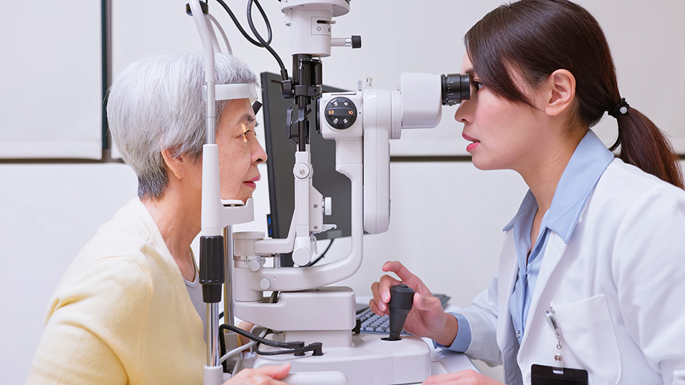 Elderly Asian woman being checked with slit lamp microscope