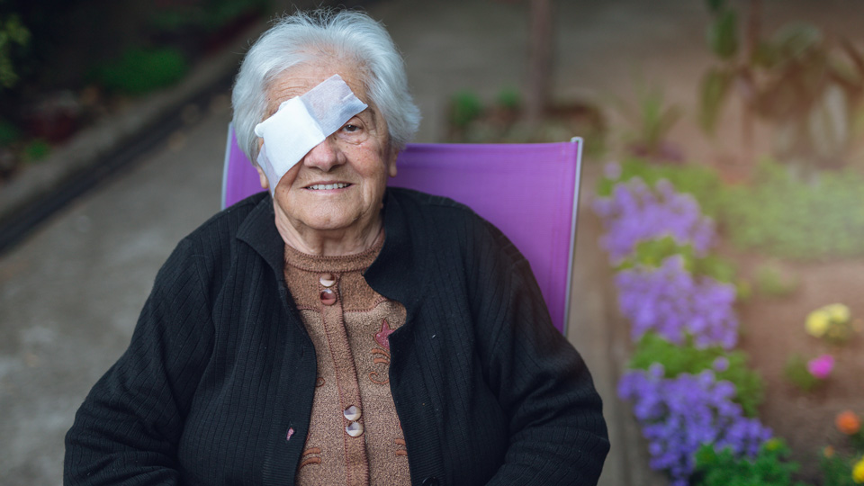 Woman sits outside wearing an eye patch bandage after a cataract operation