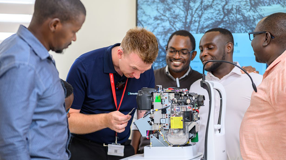 Joe Blamire leans over an OCT machine. Around him is a group of professionals he is training
